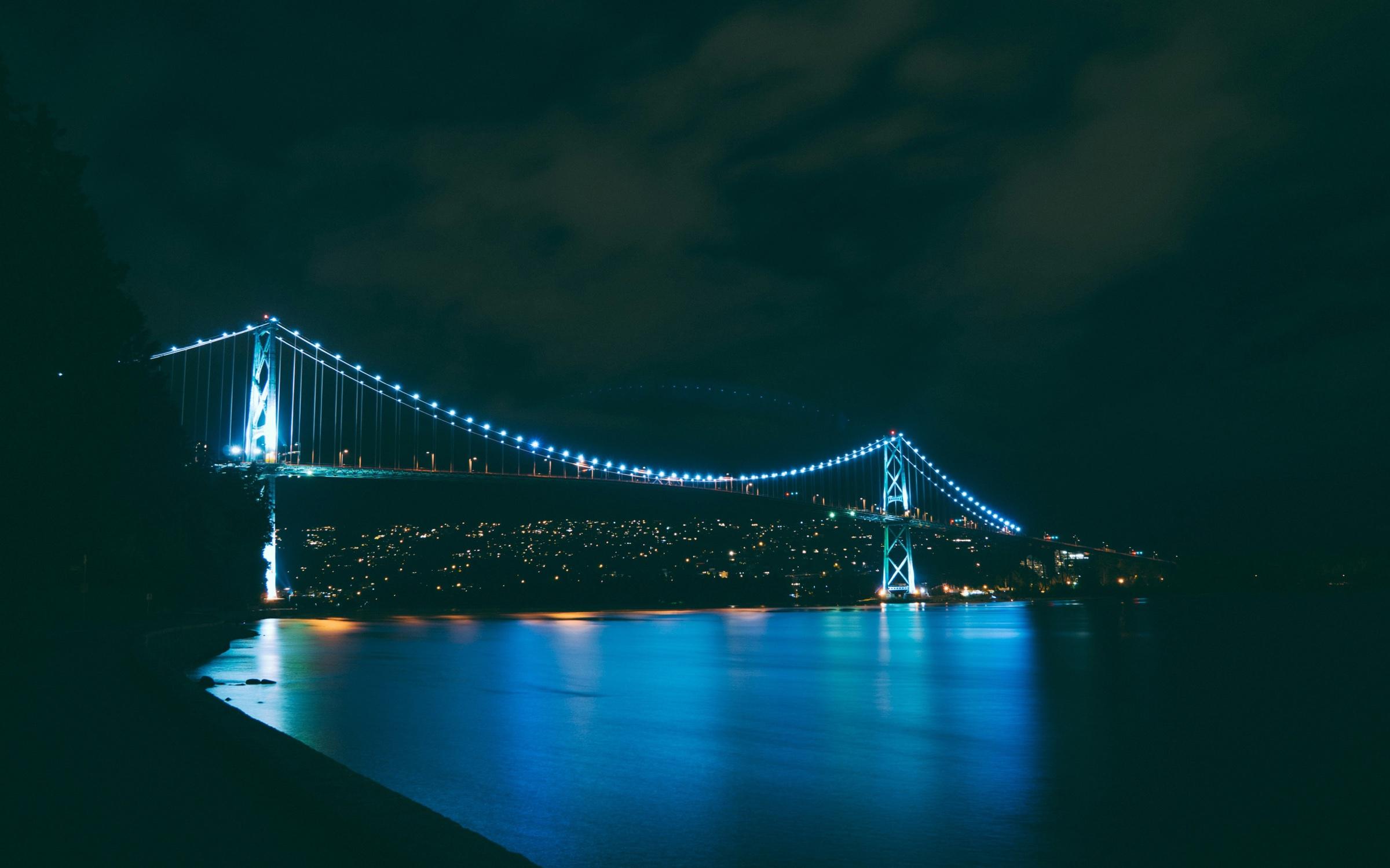 An illuminated suspension bridge connecting two shores at night
